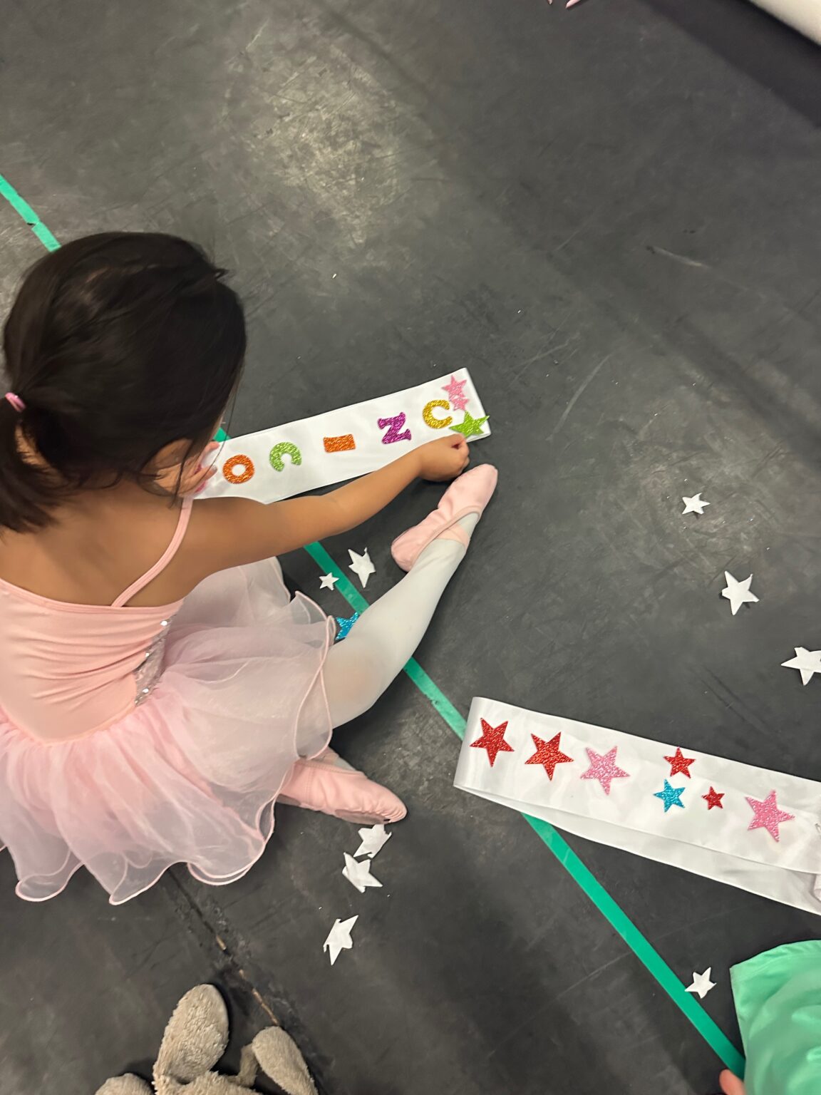 Little dancer decorating a sash with glitter stars in class